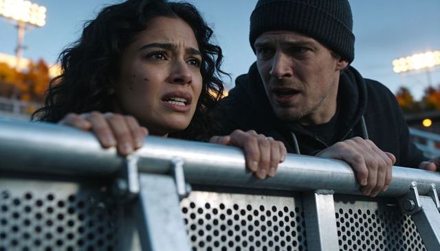 Tense couple gripping metal crowd barrier at stadium frontline during dusk