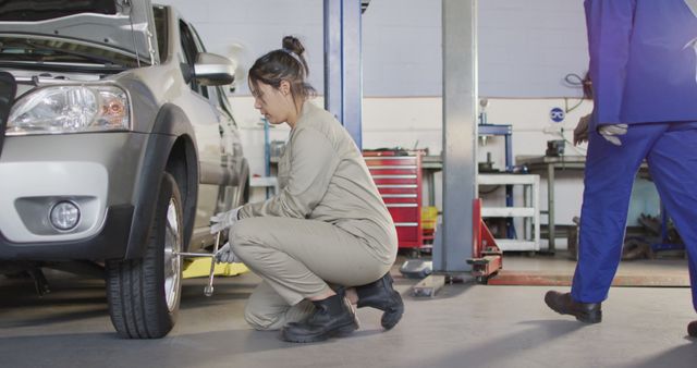 Depicts a female auto mechanic working on a car tire in a workshop garage, focusing on hands-on car maintenance. Useful for promoting gender diversity in automotive industries, showcasing vocational training, or illustrating topics related to car repair services.