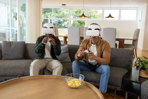 Two friends playing virtual reality games on sofa in sunlit modern living room