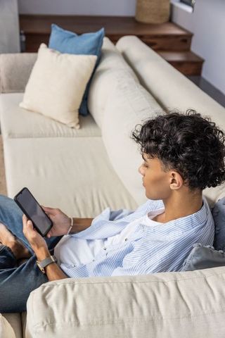 Young Man Relaxing on Sofa Using Smartphone and Wearing Smartwatch