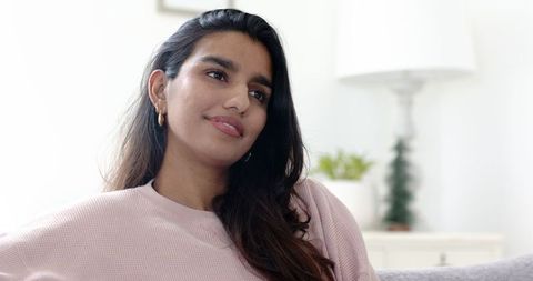 Thoughtful young indian woman relaxing in cozy living room