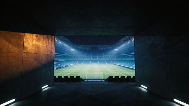 Stadium tunnel leading toward illuminated soccer pitch with centered goal and seats