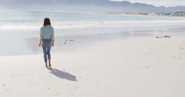 Rear view of biracial woman walking barefoot on the beach by the sea. healthy living, off the grid and close to nature.