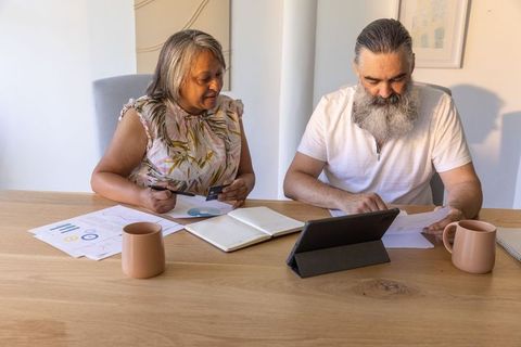 Senior couple managing household finances using tablet and charts, holding credit card