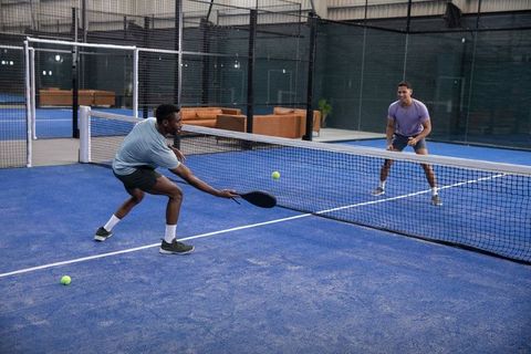 Indoor paddle sport rally with two men lunging at net on vibrant blue court