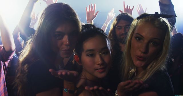 Young women of diverse ethnicities are enjoying a lively party atmosphere, with copy space. Their joyful expressions and the raised hands in the background suggest they are having a great time at a concert or club event.