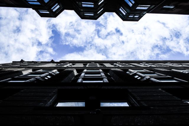 This image showcases a dramatic view from below of tall buildings against a cloudy sky. The emphasis is on the geometric facades and symmetry, creating a strong visual impact. Ideas for usage include urban lifestyle articles, architectural blogs, futuristic design features, and presentations. It can also be used as background imagery for websites and graphic design projects.