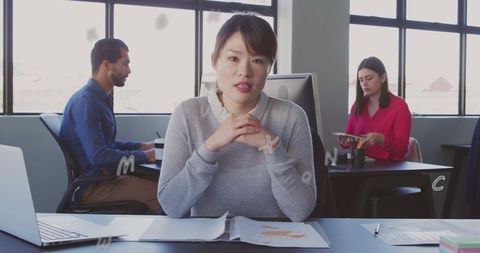 Female professional speaking at desk leading team discussion in bright open-plan workspace