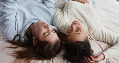 Two friends lying on bed sharing quiet moment in cozy sweaters, overhead perspective