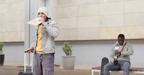 Urban travelers waiting with suitcase holding envelope while companion checking phone
