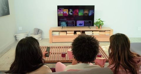 Female friends enjoying cozy movie night on sofa with popcorn and streaming tv