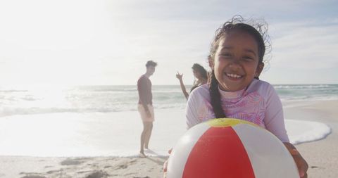 Joyful Hispanic Girl Embracing Beach Ball with Family Nearby - Download Free Stock Images Pikwizard.com
