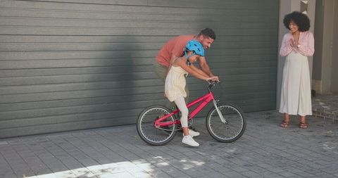 Father Teaching Daughter to Ride Bicycle on Sunny Driveway