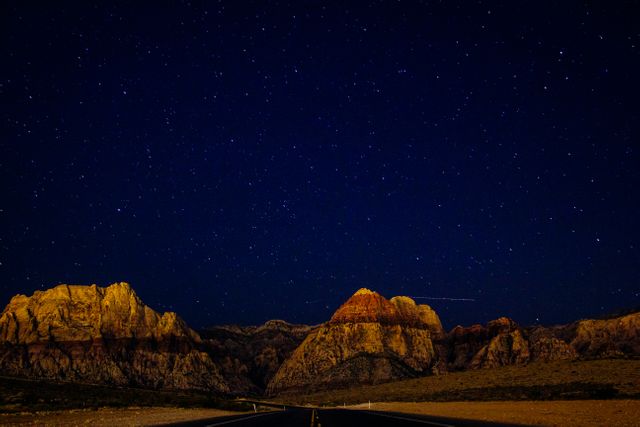 Starry sky spreads over rocky mountains at night. Dramatic desert landscape showcases tranquility and natural beauty. Perfect for backgrounds, travel blogs, adventure posters, and nature-inspired content.