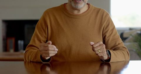 Senior man in brown sweater gesturing at home