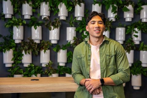 Smiling young man leaning on wooden counter in coworking space with vertical plant wall