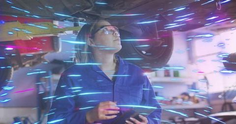 Asian mechanic inspecting undercarriage with digital tablet in workshop