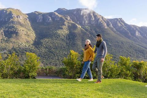 Asian couple walking on grassy overlook near mountain foothills wearing scarves and beanie