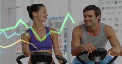 Couple Pedaling on Exercise Bikes with Cardio Metrics Overlay, Smiling and Interacting