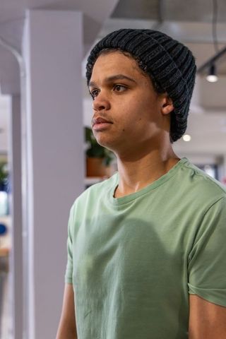 African american teen wearing beanie standing in modern cafe, casual green t-shirt, coworking