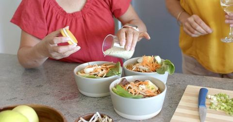 Multigenerational women preparing healthy grain bowls, pouring seeds and assembling fresh salads
