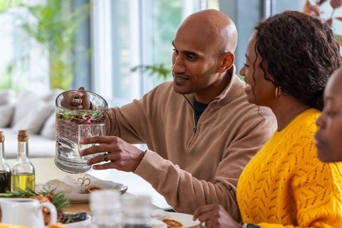 Diverse family pouring citrus and herb infused water at bright home dining table