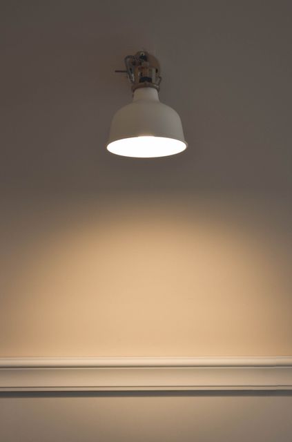Image focusing on a modern white wall light illuminating an empty beige wall, creating a minimalist aesthetic. This photo can be used for blog posts or articles related to home decor, interior design tips, or lighting solutions. It is also suitable for brochures, advertisements, or websites promoting modern or contemporary home lighting products.