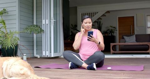 Mature woman practicing mindfulness on patio using smartphone and earbuds with dog