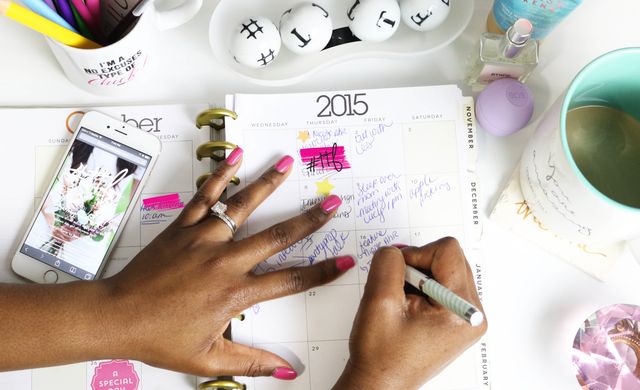Woman writing in 2015 planner, organizing her schedule on desk. Ideal for illustrating themes of productivity, daily planning, time management. Featuring a cozy desk arrangement with smartphone, coffee, stationery. Perfect for articles about personal organization, productivity hacks, planner brands.