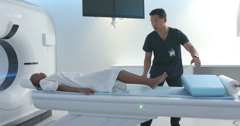 Asian technician positioning black patient for ct scan in modern radiology suite