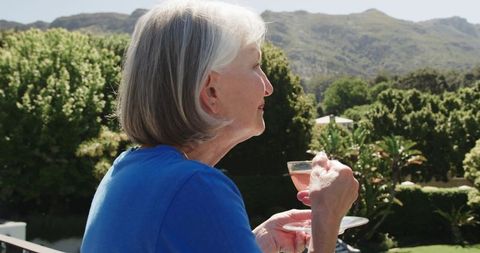 Senior woman enjoying wine on balcony overlooking scenic view