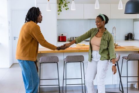 African american couple holding hands at modern kitchen island, sunlit minimalist interior