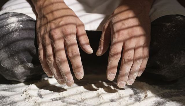 Baker hands dusted with flour hovering above dough-sprinkled surface in striped sunlight