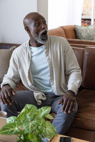 Surprised senior african american man sitting on leather couch reacting to phone at home