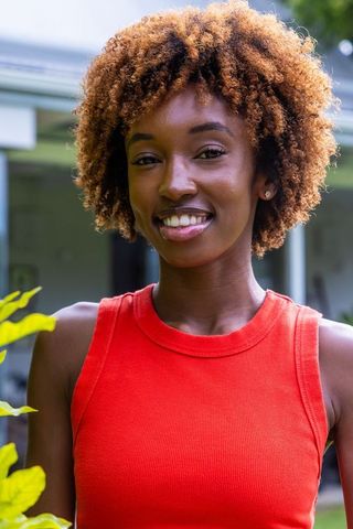 Smiling african american woman posing on porch wearing red tank top and stud earrings