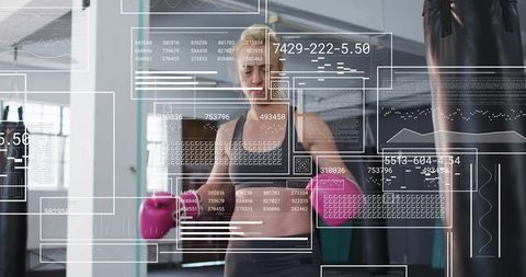 Woman boxer training with hud overlay punching heavy bag in gym wearing pink gloves
