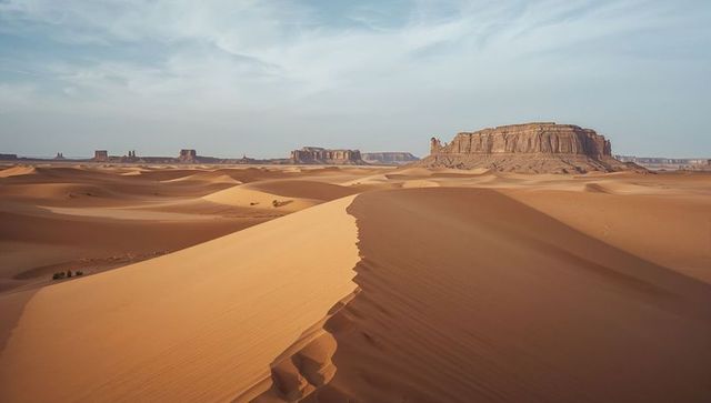 Shifting sand dune ridge curving toward distant sandstone mesas in windswept desert basin
