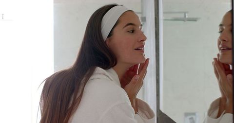 Young woman performing mirror skincare routine in bathroom