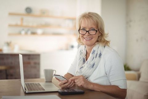 Senior Woman Smiling at Kitchen Table with Smartphone and Laptop - Download Free Stock Images Pikwizard.com