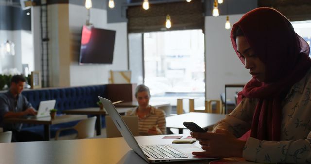 Woman in Hijab Using Smartphone and Laptop in Modern Cafe - Download Free Stock Images Pikwizard.com