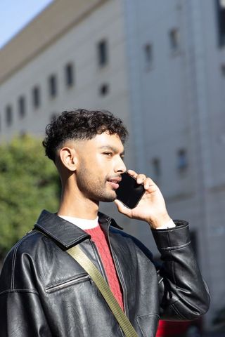 Indian man mid-20s talking on smartphone in leather jacket on urban street