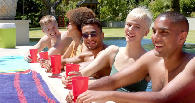 Portrait of happy diverse friends drinking drinks at pool party in summer. Friendship and spending quality time at home concept.