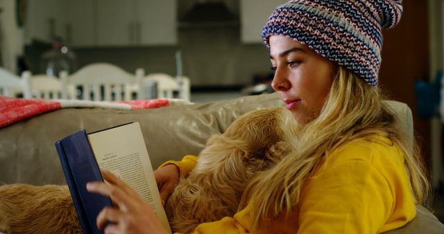 Young woman enjoying a cozy moment at home, reading a book with her dog on the couch. Perfect for concepts related to relaxation, leisure time, bonding with pets, and everyday life indoors. Great for use in blogs, articles, and ads promoting home comforts and casual lifestyle.