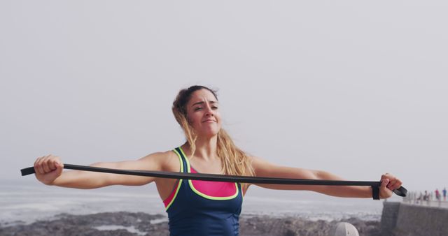 Woman exercising with resistance band outdoors near ocean - Download Free Stock Images Pikwizard.com