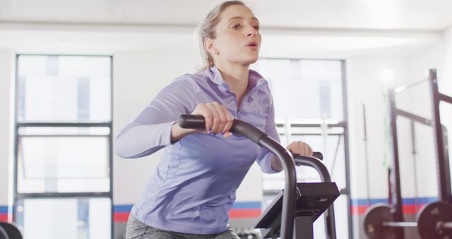 Woman wearing athletic wear using a stationary bike in a bright, modern gym. Emphasizing physical fitness, healthy lifestyle, and regular exercise. Useful for promoting gym memberships, fitness programs, or content related to health and fitness.
