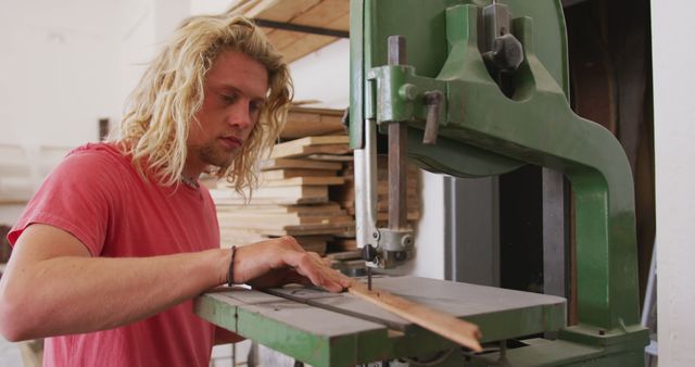 Caucasian male surfboard maker concentrating, cutting wood with jigsaw at workshop, unaltered. Small business, work, sports equipment and craftsmanship.