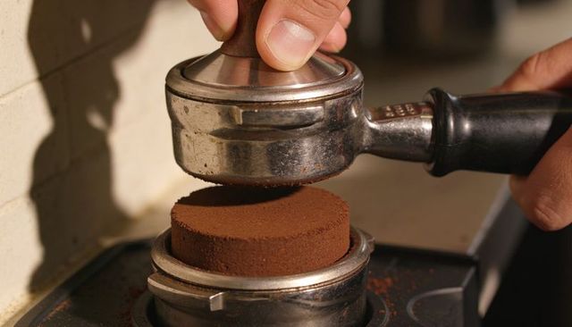 Barista pressing tamper, steadying portafilter with freshly ground espresso puck in cafe