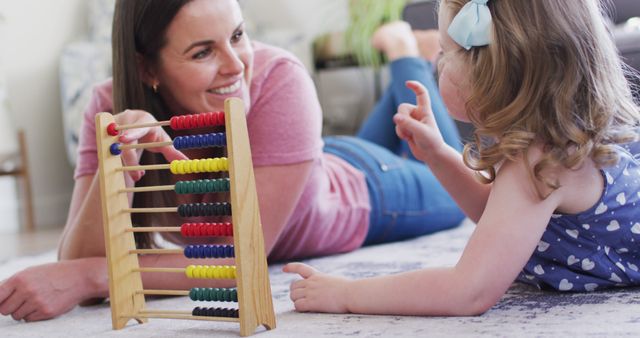 Mother and young daughter playing and learning together with a colorful abacus in a cozy living room. Ideal for educational content, parenting blogs, or advertisements focused on family bonding and early childhood education.