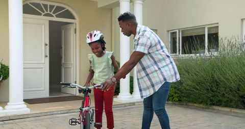 Father Teaching Daughter to Ride Bike Outside Home, Smiling Bonding Moment