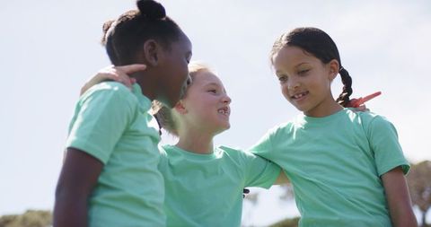 Teen girls linking arms in park wearing matching mint green t-shirts